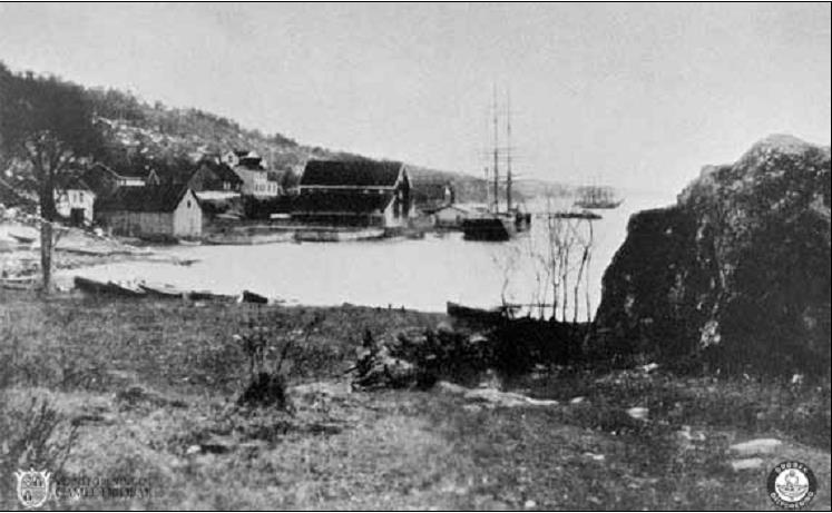 Båthavna 1895. Ishus og Jacob Carlsens sjøbod er dominerende i bukta, med lav  trehusbebyggelse bak. Strendene var lagerplass for tønner, bjelker og plank. (Bildebehandling: Joar Foto)